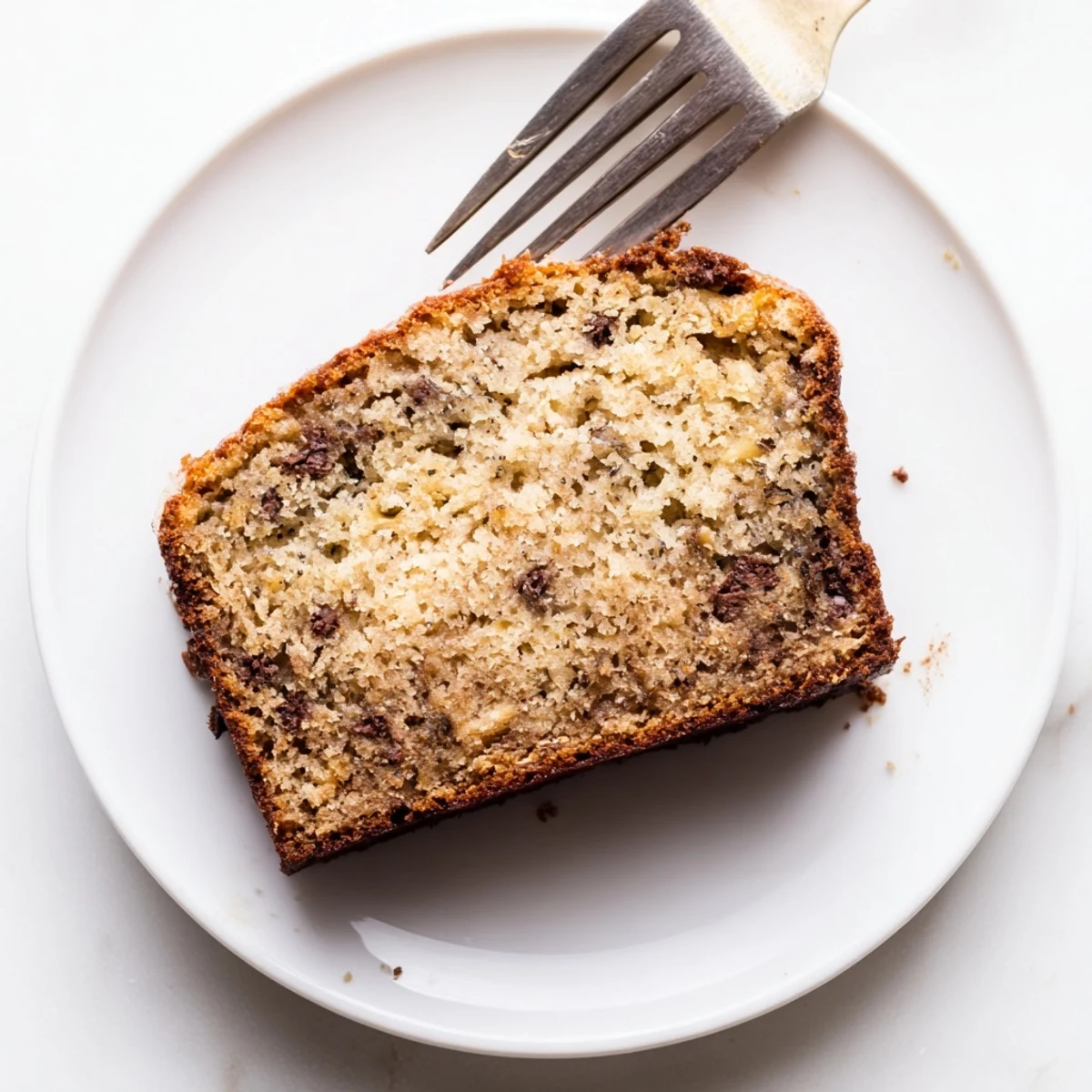 Slice of moist banana bread with sour cream topped with melting butter on a white plate