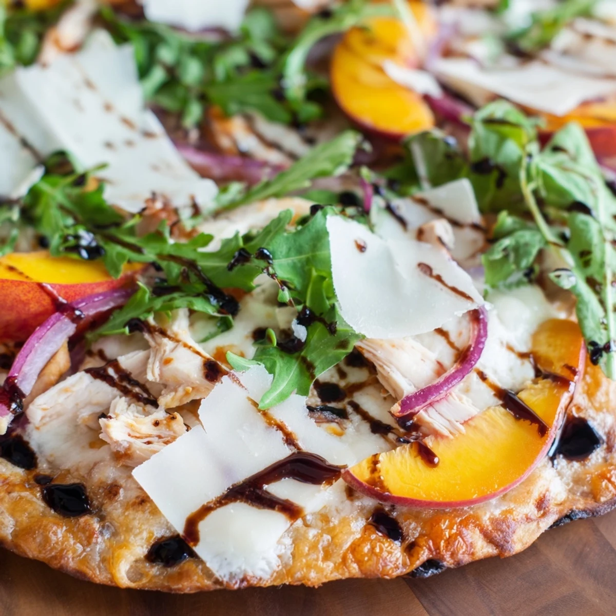 Sliced chicken peach ricotta pizza finished with fresh arugula and sweet balsamic glaze