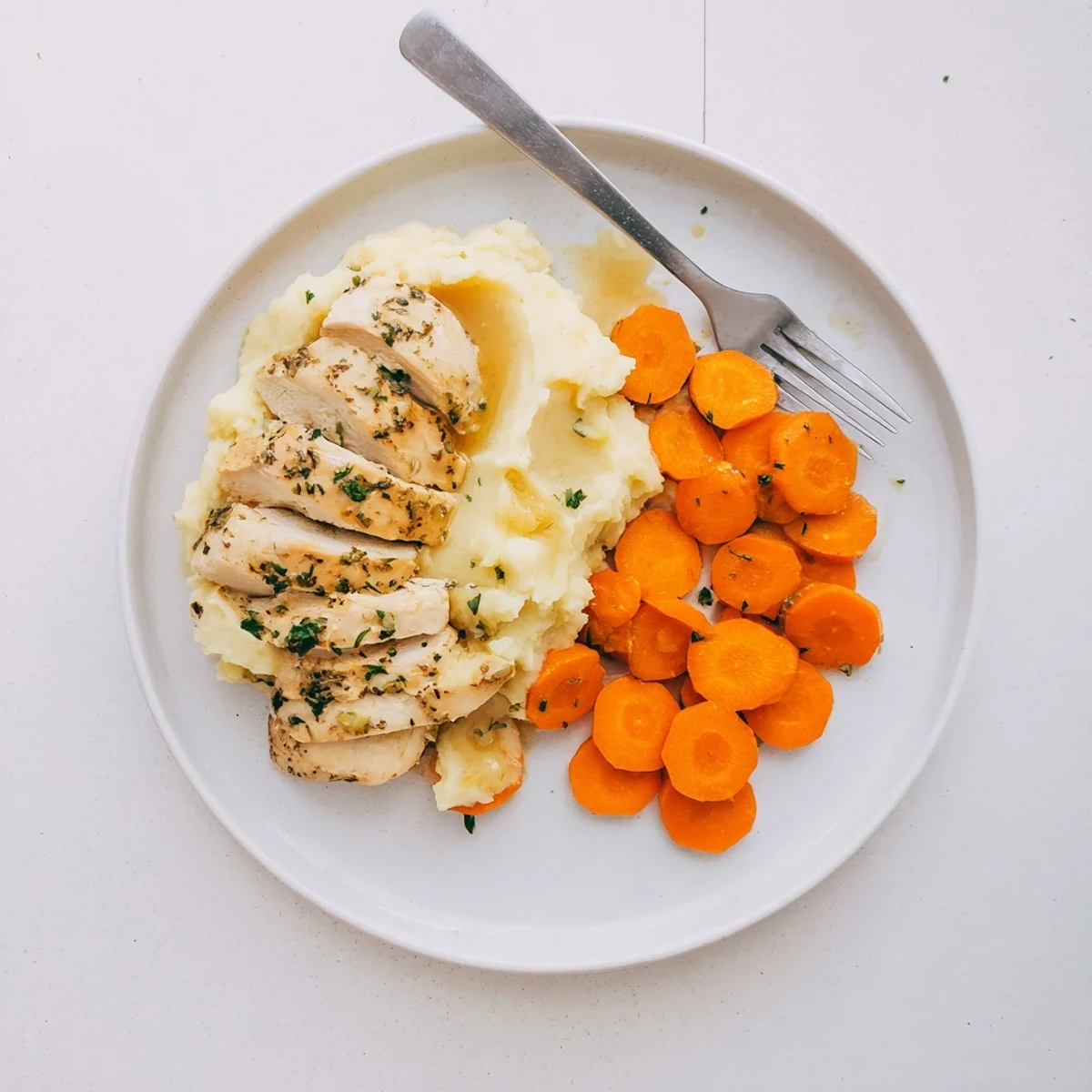 Tender marinated chicken served with velvety mashed potatoes and sweet buttery glazed carrots on white plate