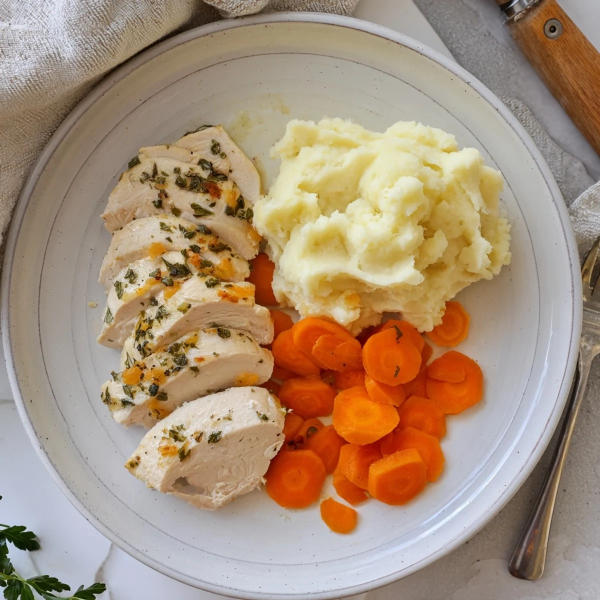 Garlic herb chicken resting on creamy mashed potatoes with shiny glazed carrots and fresh parsley garnish