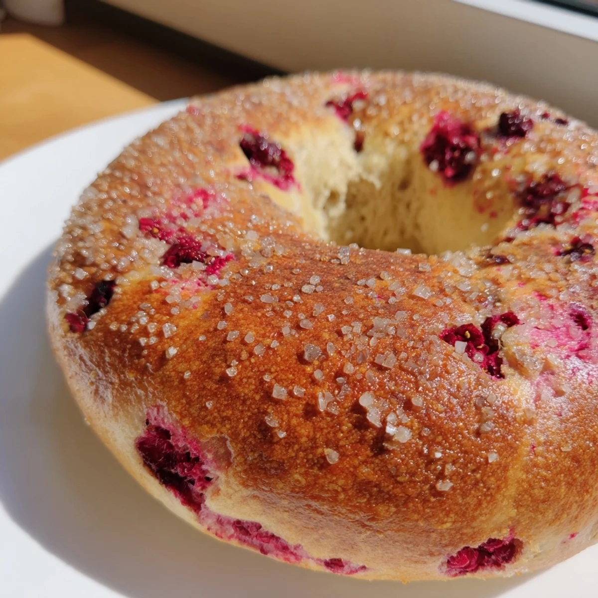 Chewy artisan bagel swirled with tart raspberries on a wooden cutting board