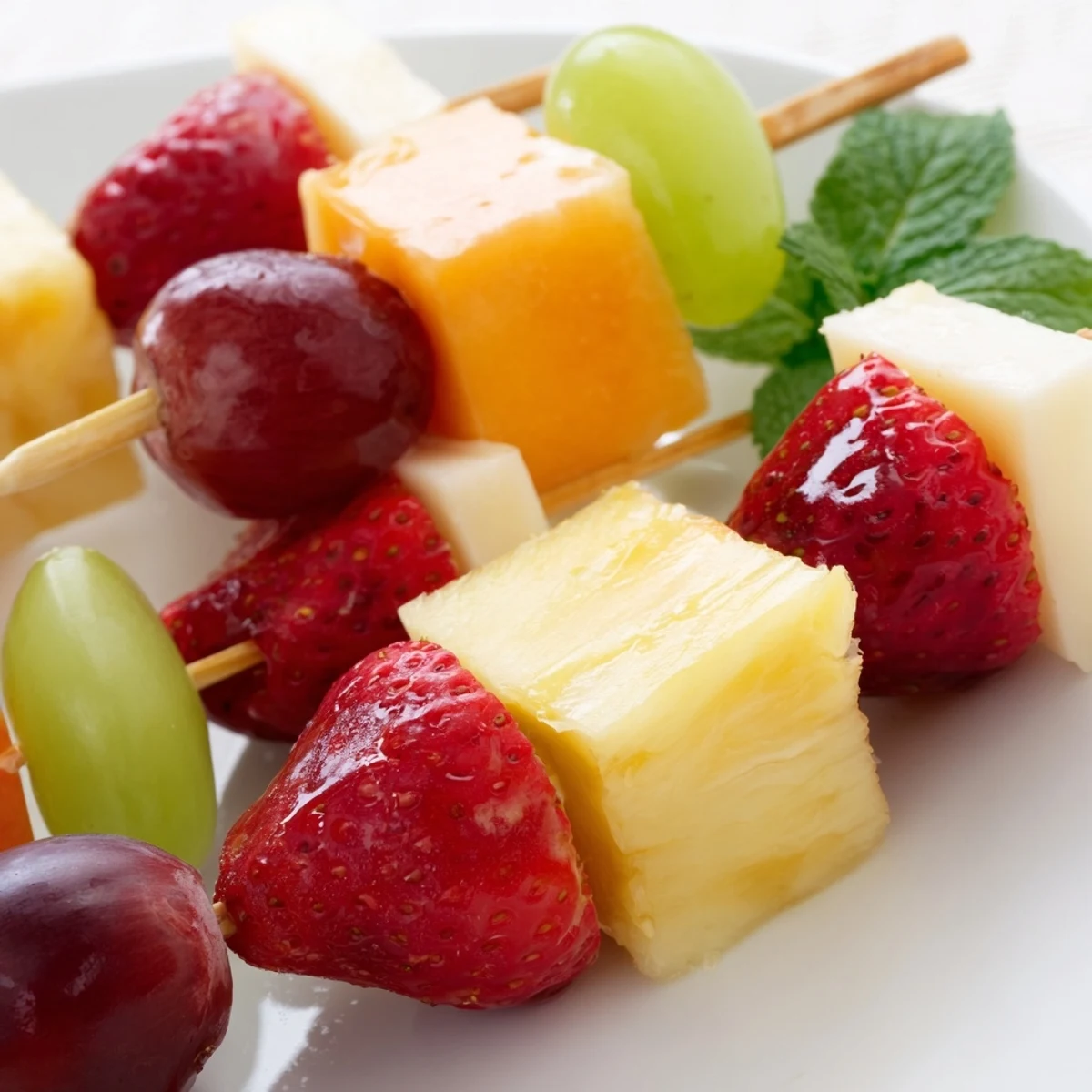 Fruit and cheese kabobs featuring alternating red grapes mozzarella and pineapple on wooden skewers
