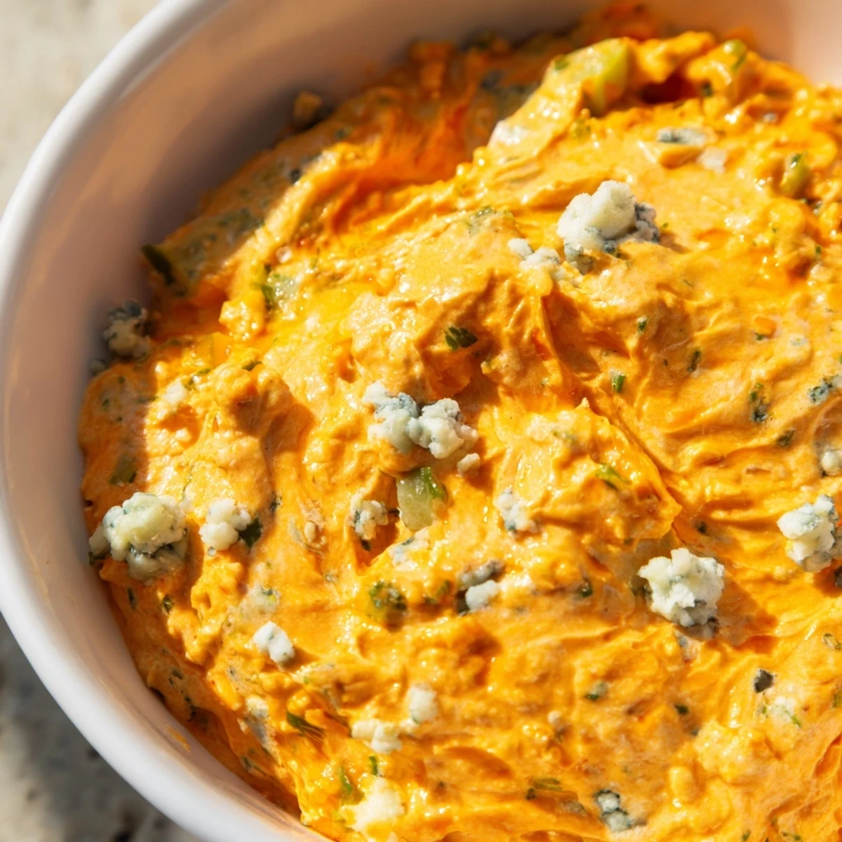 Creamy buffalo pickle dip in a serving bowl surrounded by crunchy chips and fresh veggie sticks