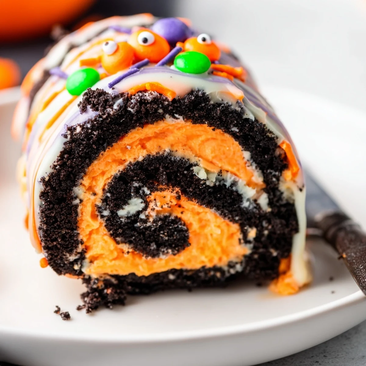 A slice of Halloween Oreo Roll topped with candy eyes and orange sprinkles on a festive plate
