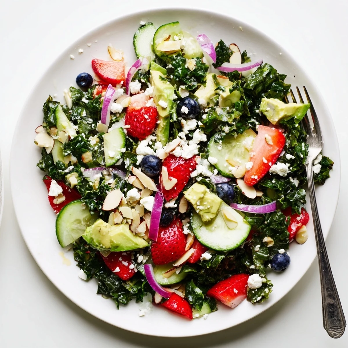 Colorful summer kale salad topped with fresh berries, feta, and toasted almonds