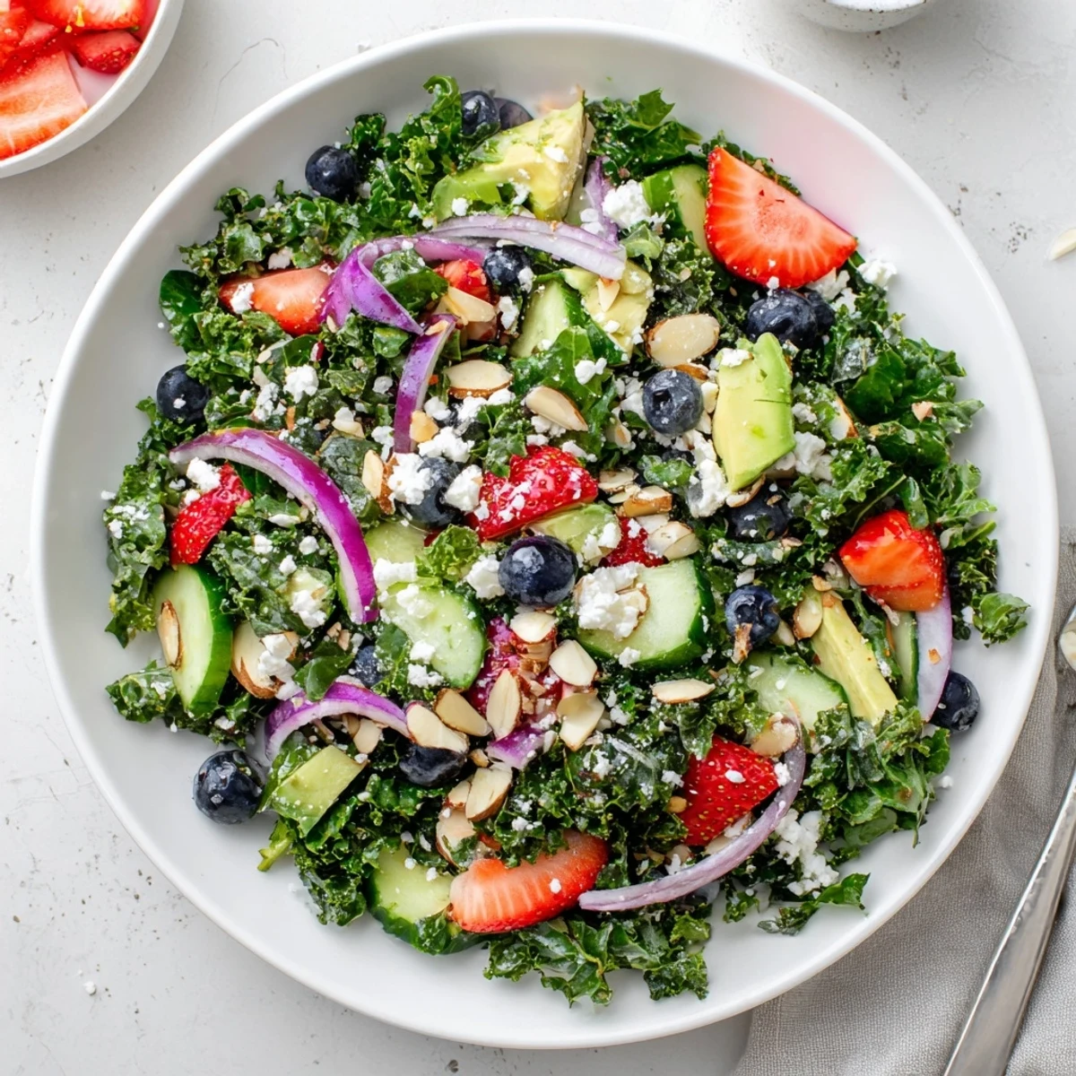 Hearty summer kale salad with juicy strawberries and creamy avocado on a white plate