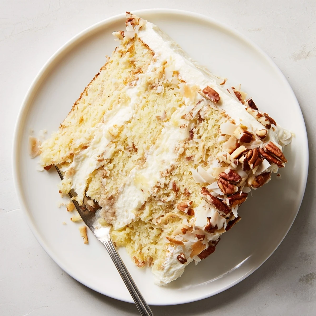 Frosted Quick Italian Cream Cake sprinkled with crunchy pecans and sweet coconut on a serving plate