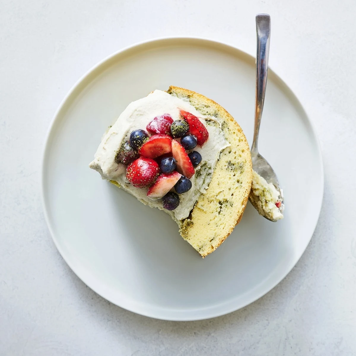 Golden basil berry cake slice topped with vibrant red berry compote and green basil whipped cream