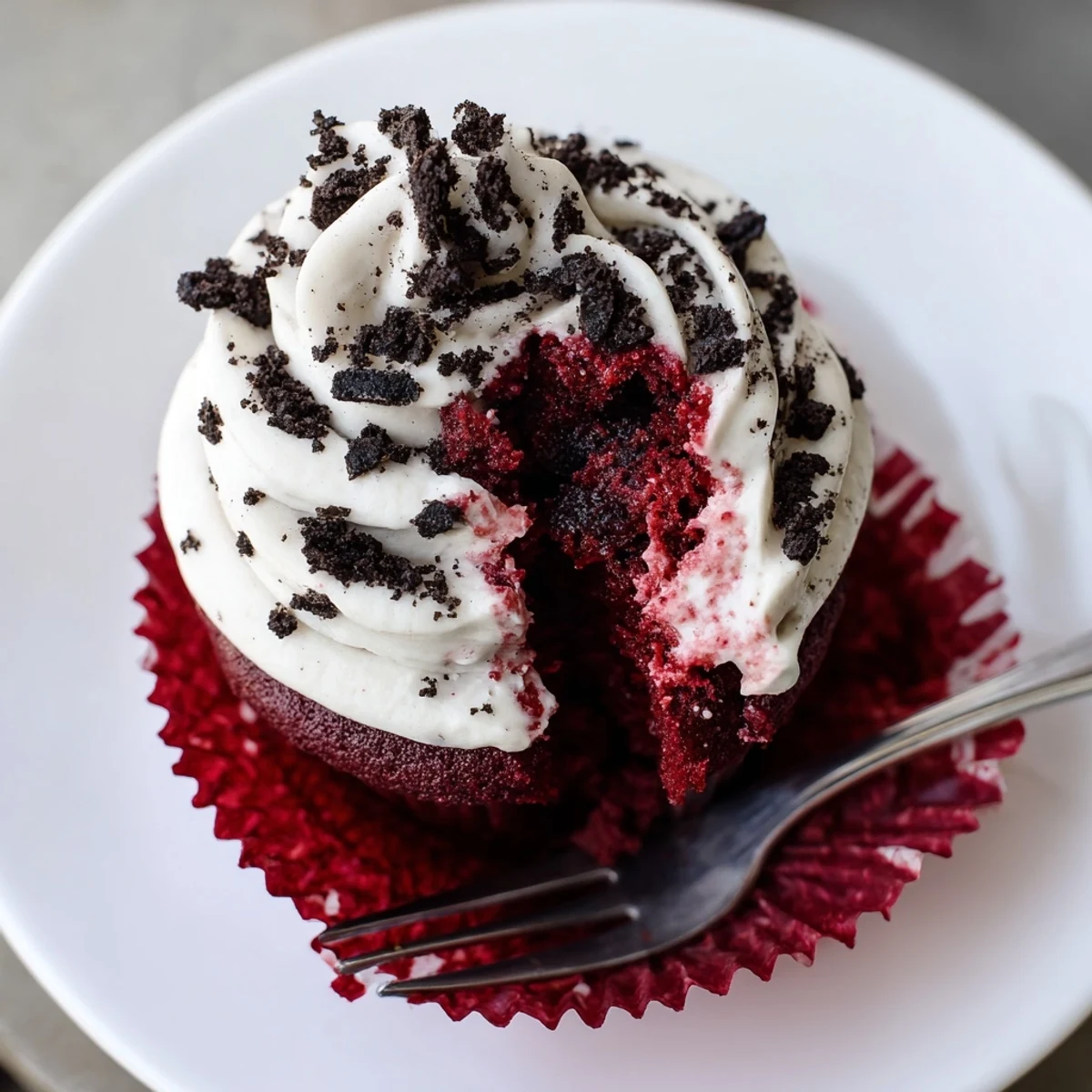 Red Velvet Oreo Cupcakes topped with creamy frosting and cookie crumbs on a rustic plate